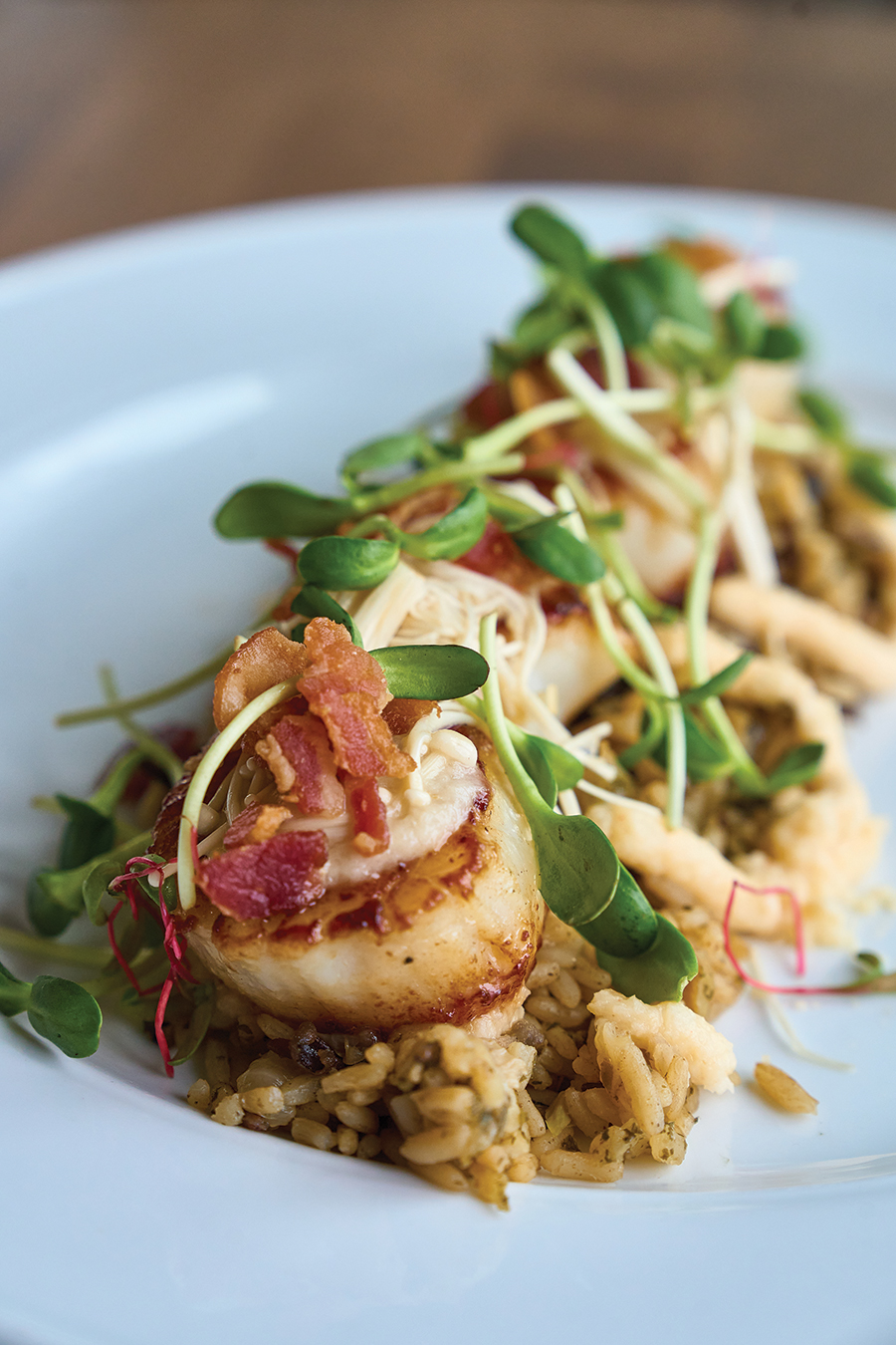 Pan-seared scallops are accompanied with celery root, bacon lardons, pickled enoki mushrooms, wild rice and a caramelized onion puree.