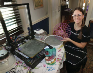 Natalie Ashton with her 3D printer and one of the parts she produces to help incubate chickens.