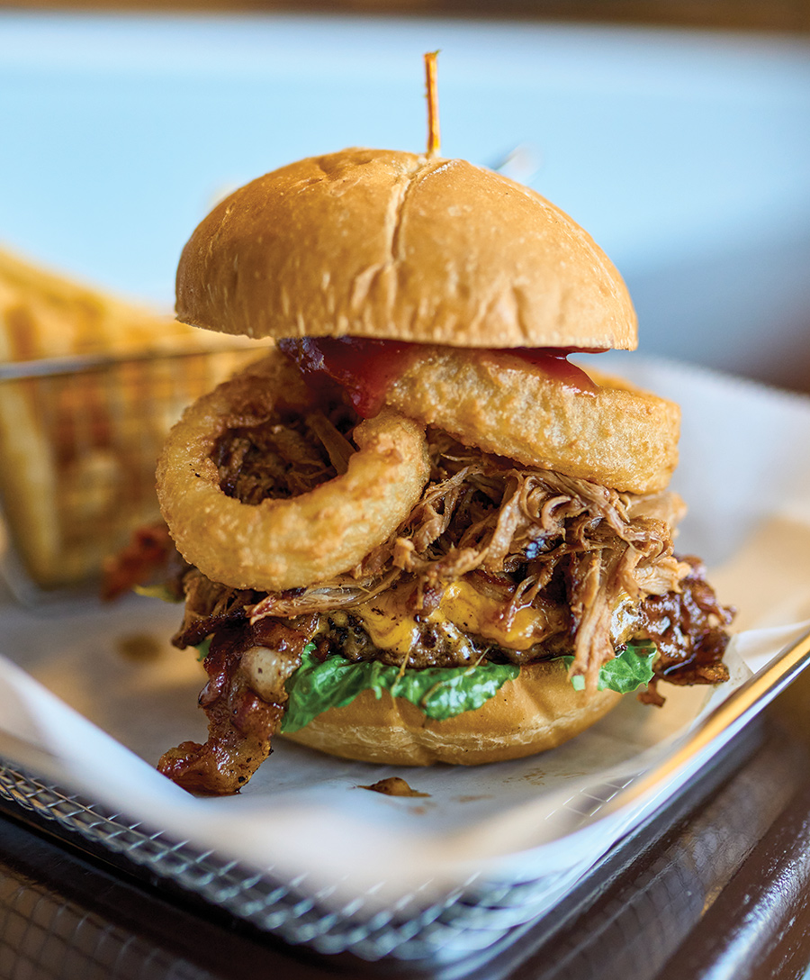 The Dirty Burger features a cheddar-topped beef patty piled with BBQ pulled pork, thick cut hickory bacon and fried onion rings.