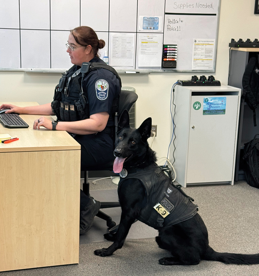 Officer Wilhelm sits at her desk with Ghost beside her.