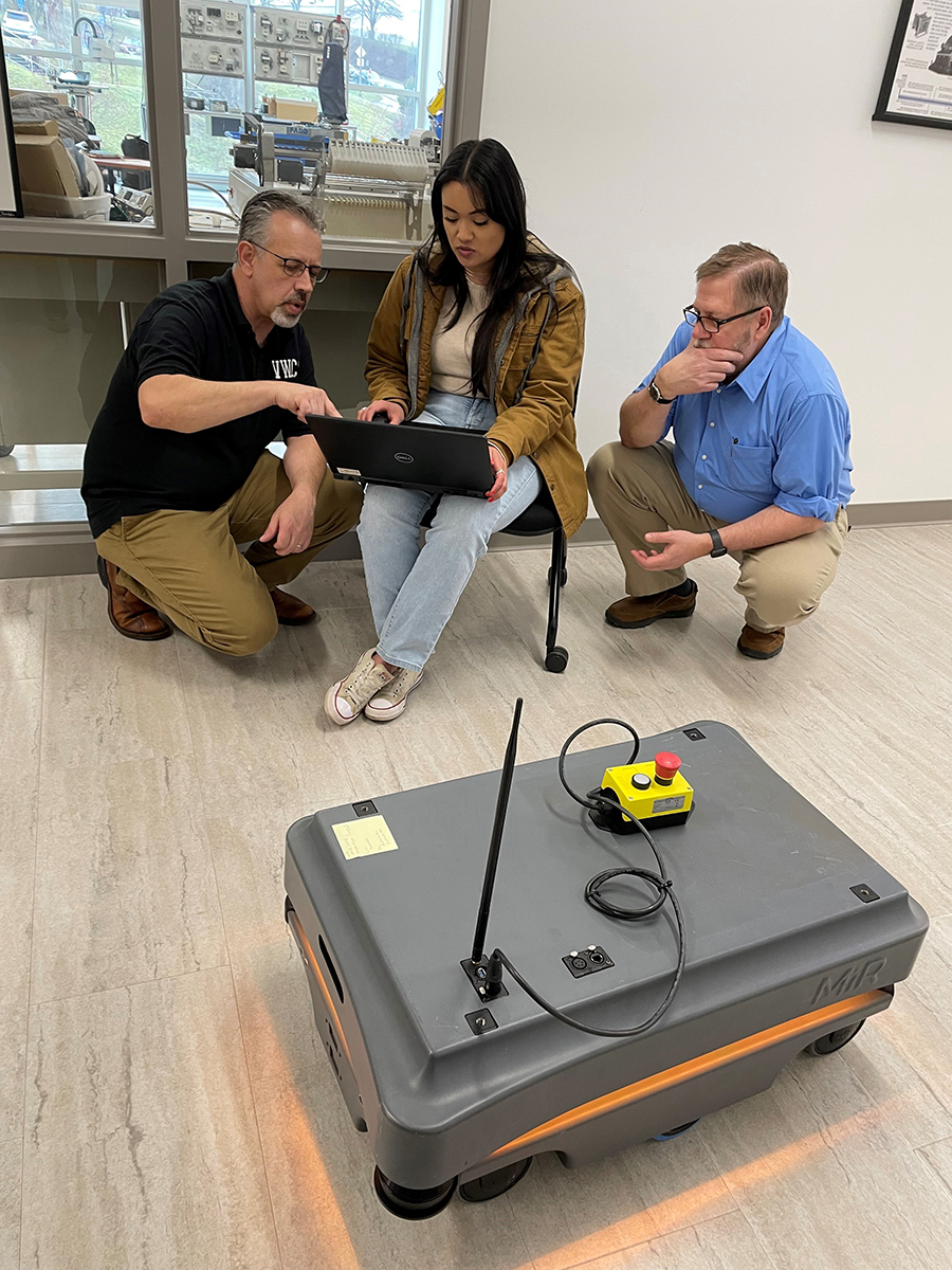 Dr. David Berry (left) helps Briana Wood and Adam O’Neal as the class fine-tunes a map of the STEM Building’s hallway for the MiR 2000, a mobile industrial robot. A strip of light around the base emits colors that follow a code, such as a purple/yellow combination for an error.