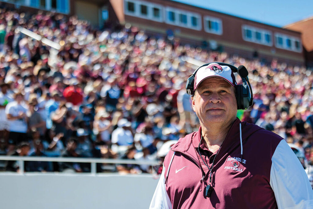 Coach Stinespring on the sideline in front of a packed stadium of spirited Roanoke College fans.