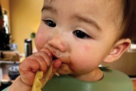 At seven months old, Colette Butto enjoys feeding herself. Colette likes meats over veggies while twin sister Scarlett prefers fruits and vegetables over meats.